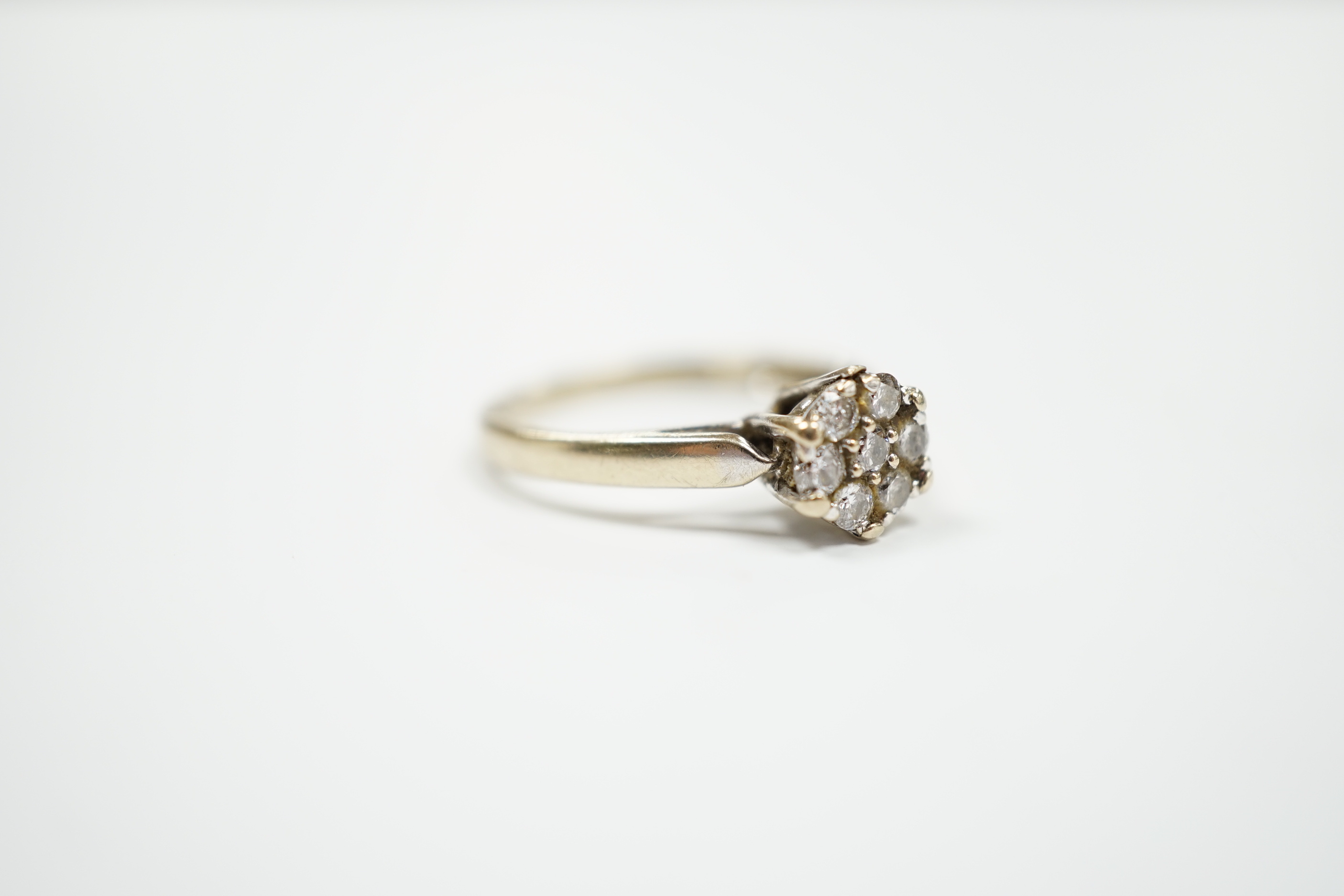 A 750 white metal and seven stone diamond set circular cluster ring, size M, gross weight 3.2 grams.